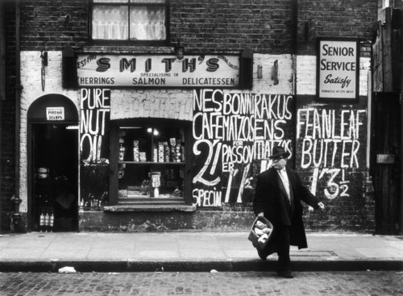 Man in an overcoat and hat crosses the road: 1961