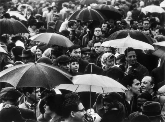 A crowd huddled underneath umbrellas in the rain: 1961